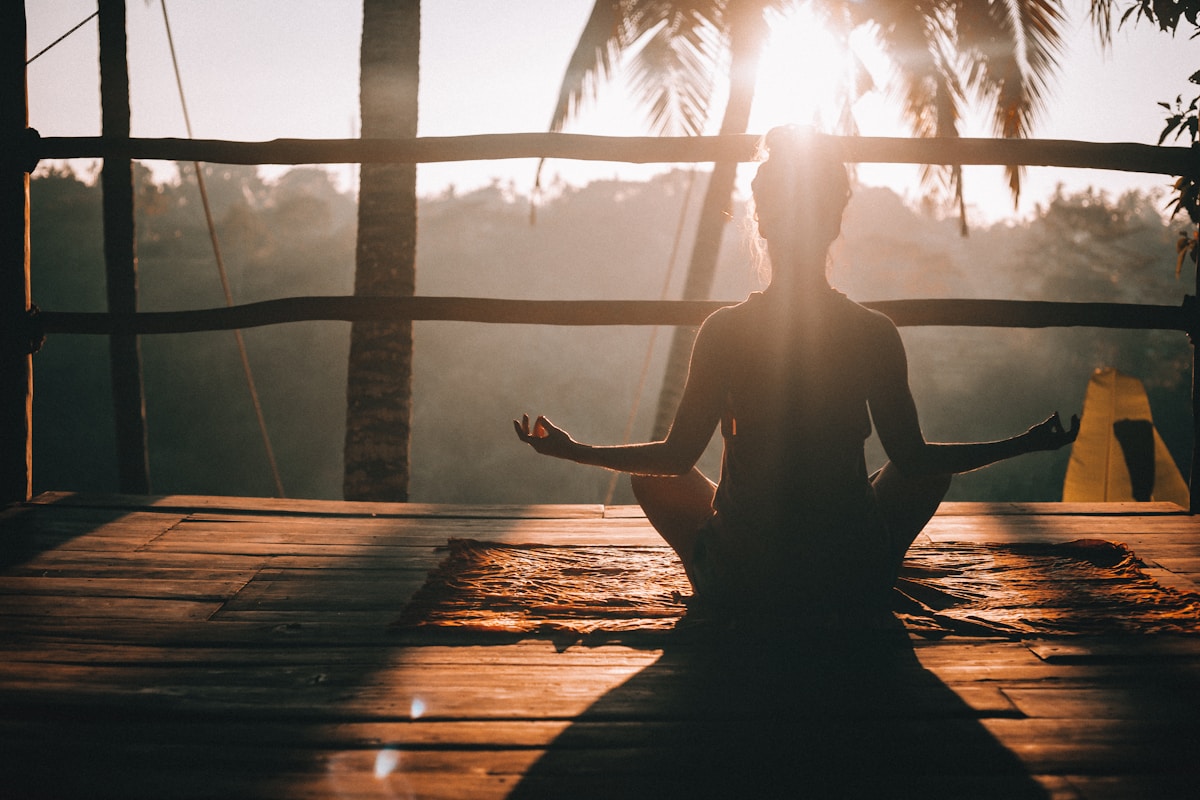 Woman meditating in lotus pose on a wooden platform at sunset, Ubud, Bali