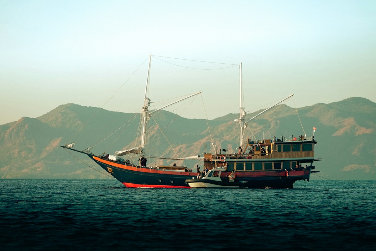 Traditional phinisi liveaboard vessel on calm water with dry rocky mountains, East Nusa Tenggara, Indonesia