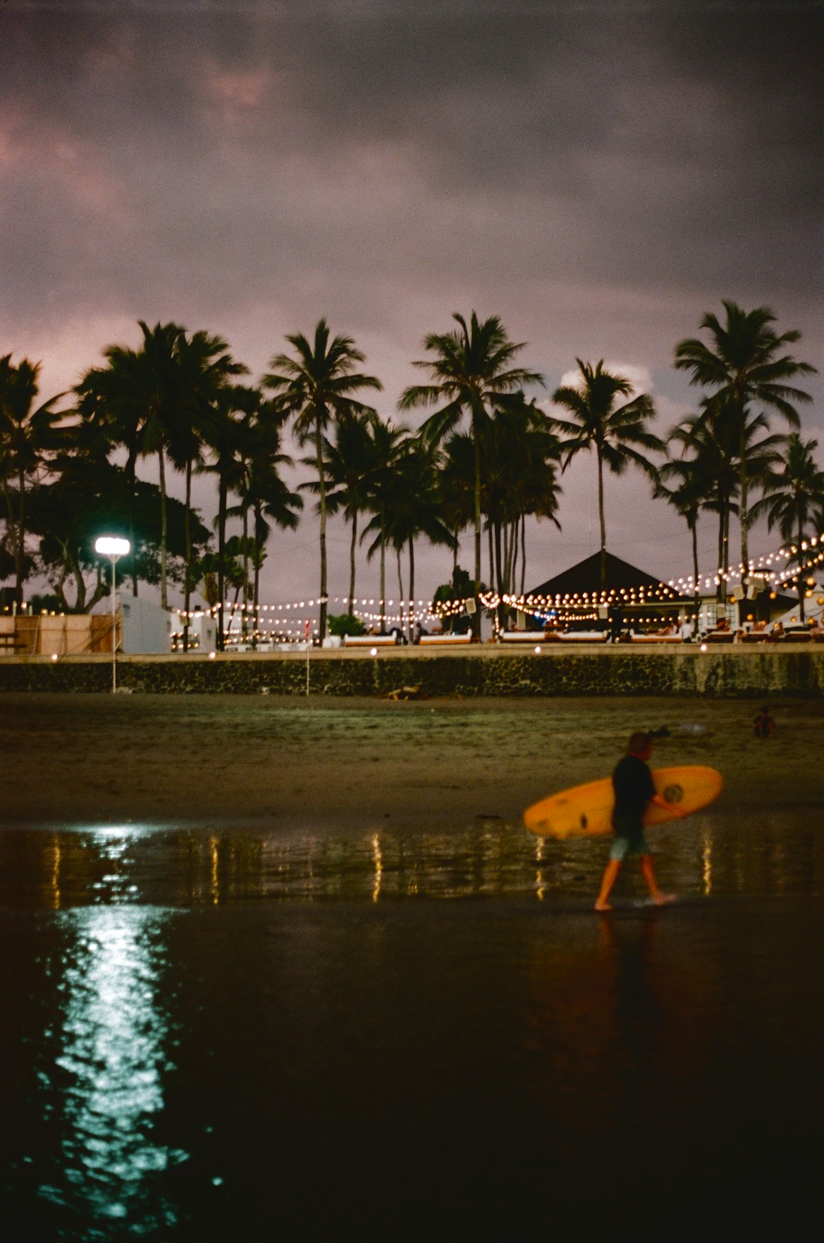 A man carrying a surfboard on a beach at night, Bali, Indonesia