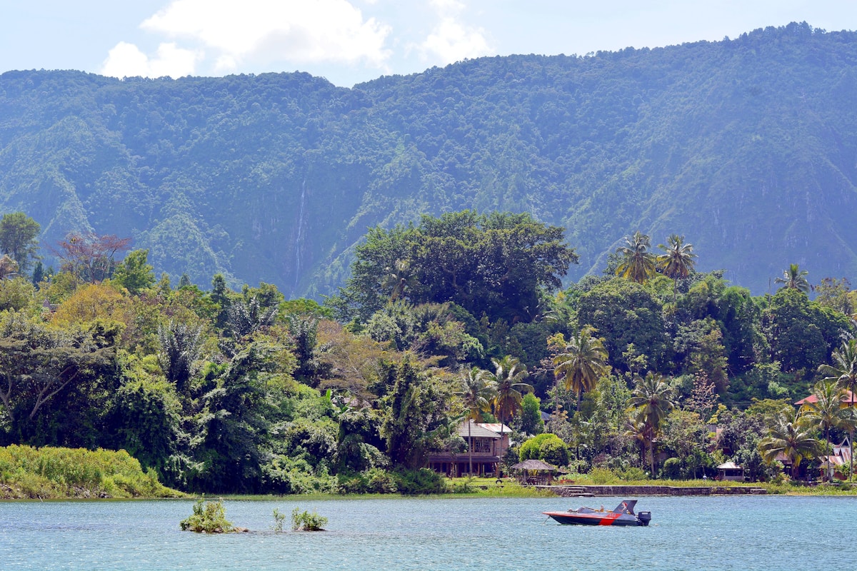 Red boat on lake near green trees and mountain, Lake Toba, Indonesia