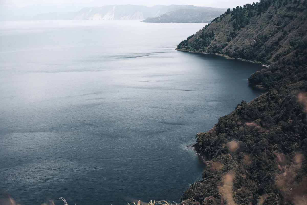 Serene lake beside green forested hill, Lake Toba, Indonesia