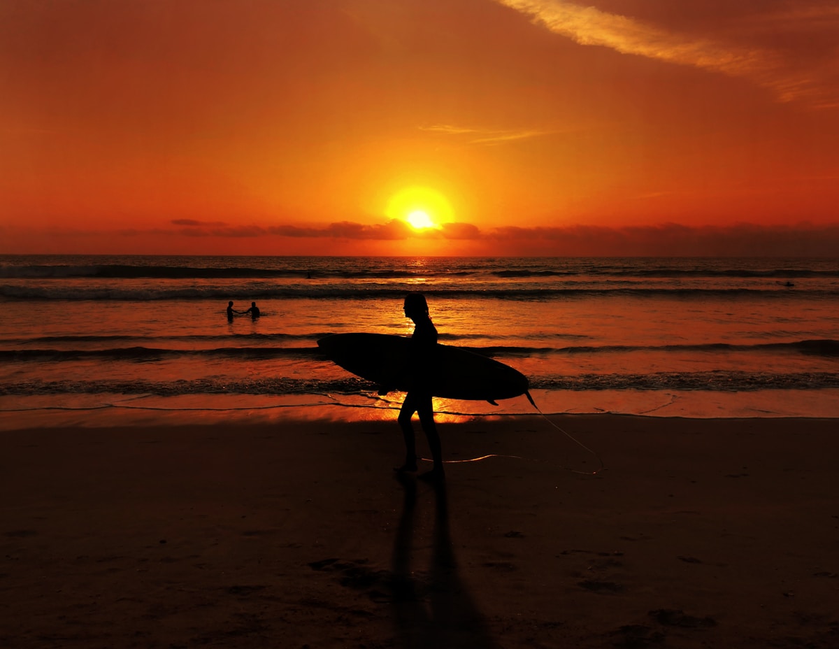 Surfer carrying a board along a Bali beach at sunset