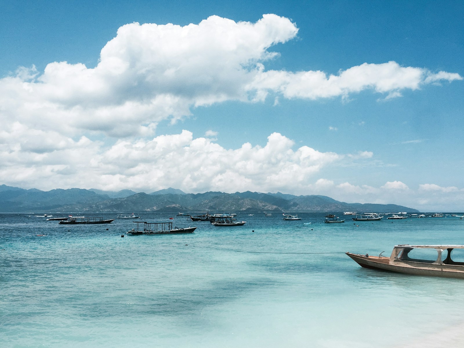 Traditional wooden boats moored in turquoise water at Gili Trawangan with Lombok mountains beyond