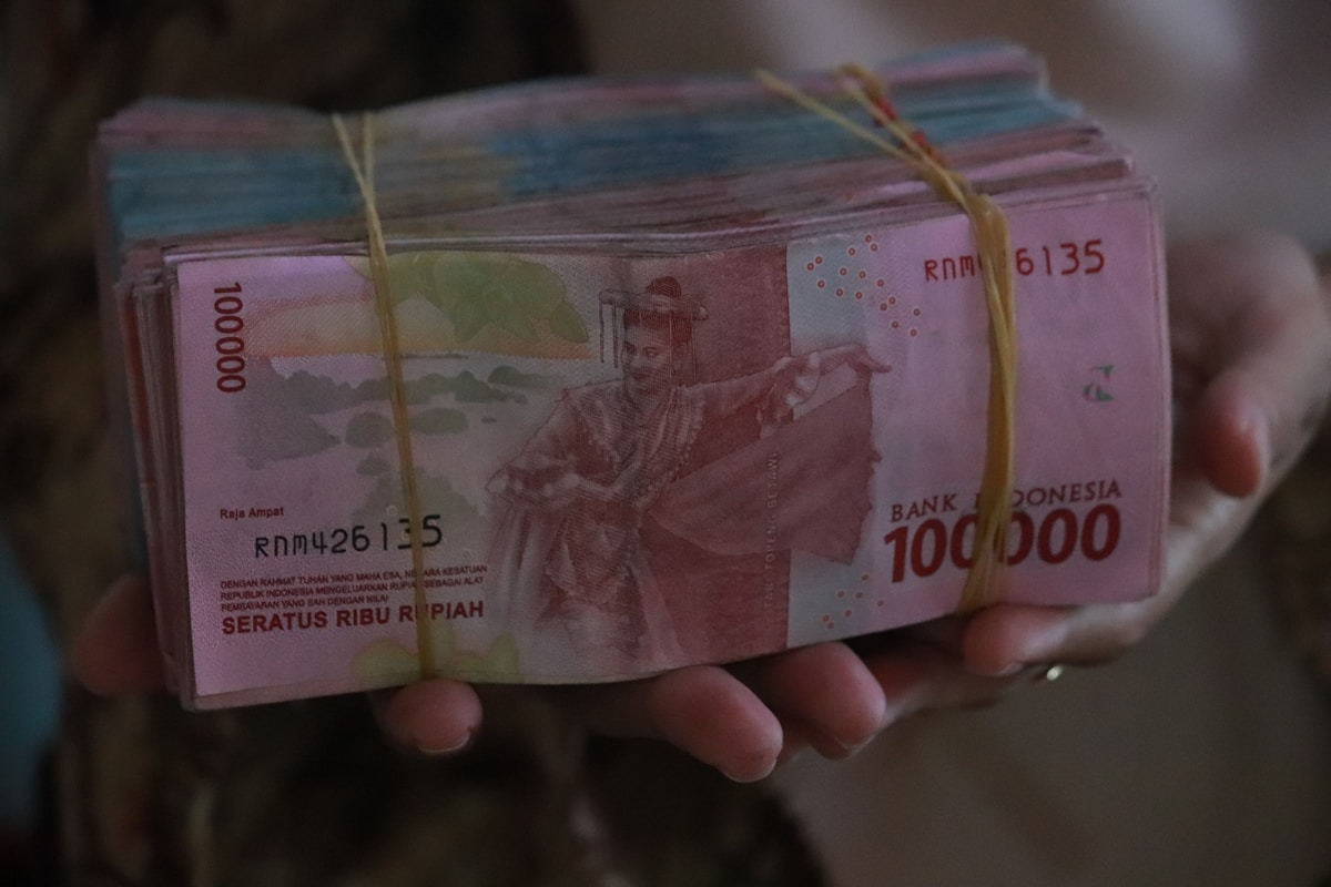 Person holding a stack of 100,000 Indonesian rupiah banknotes