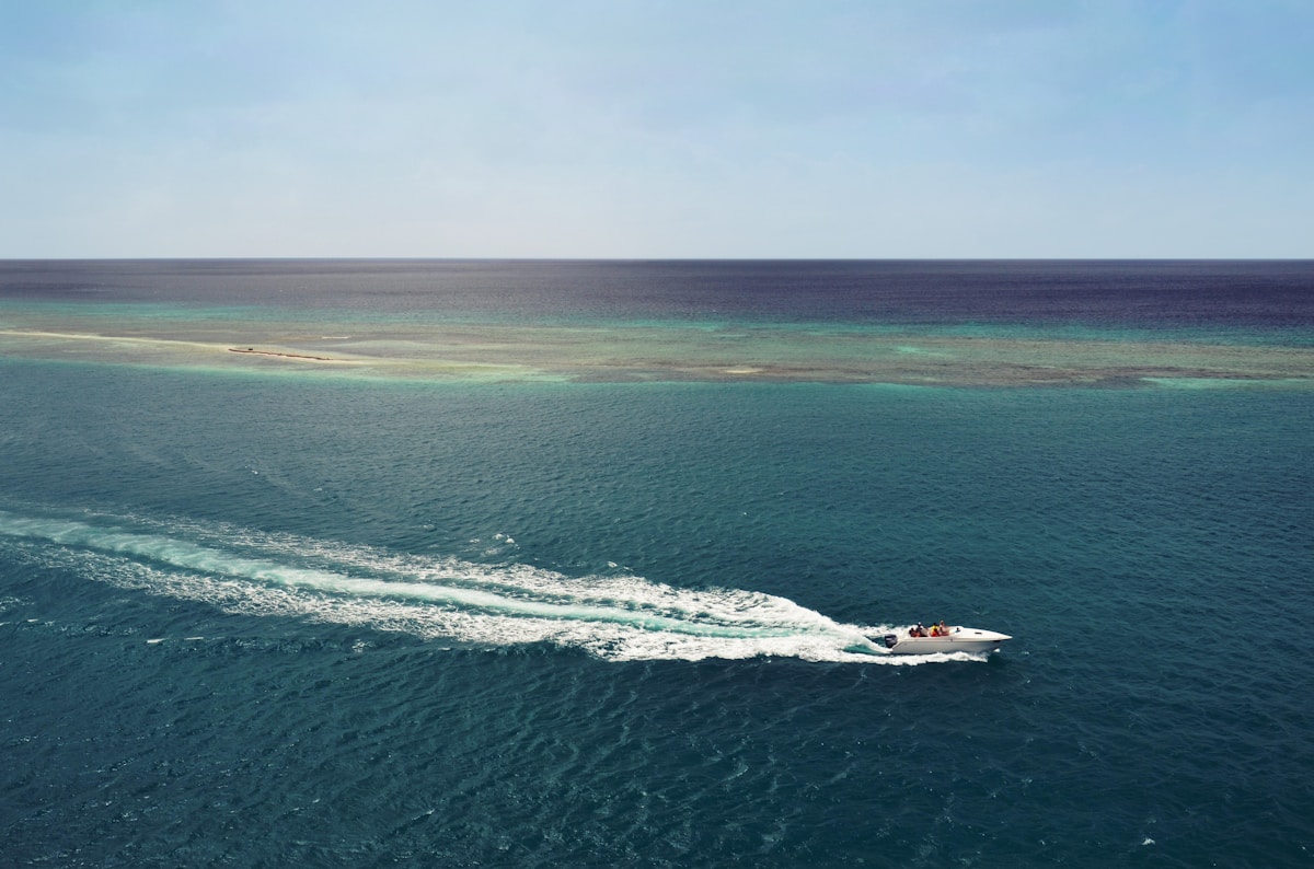 White speedboat crossing deep blue ocean toward reef, Indonesia