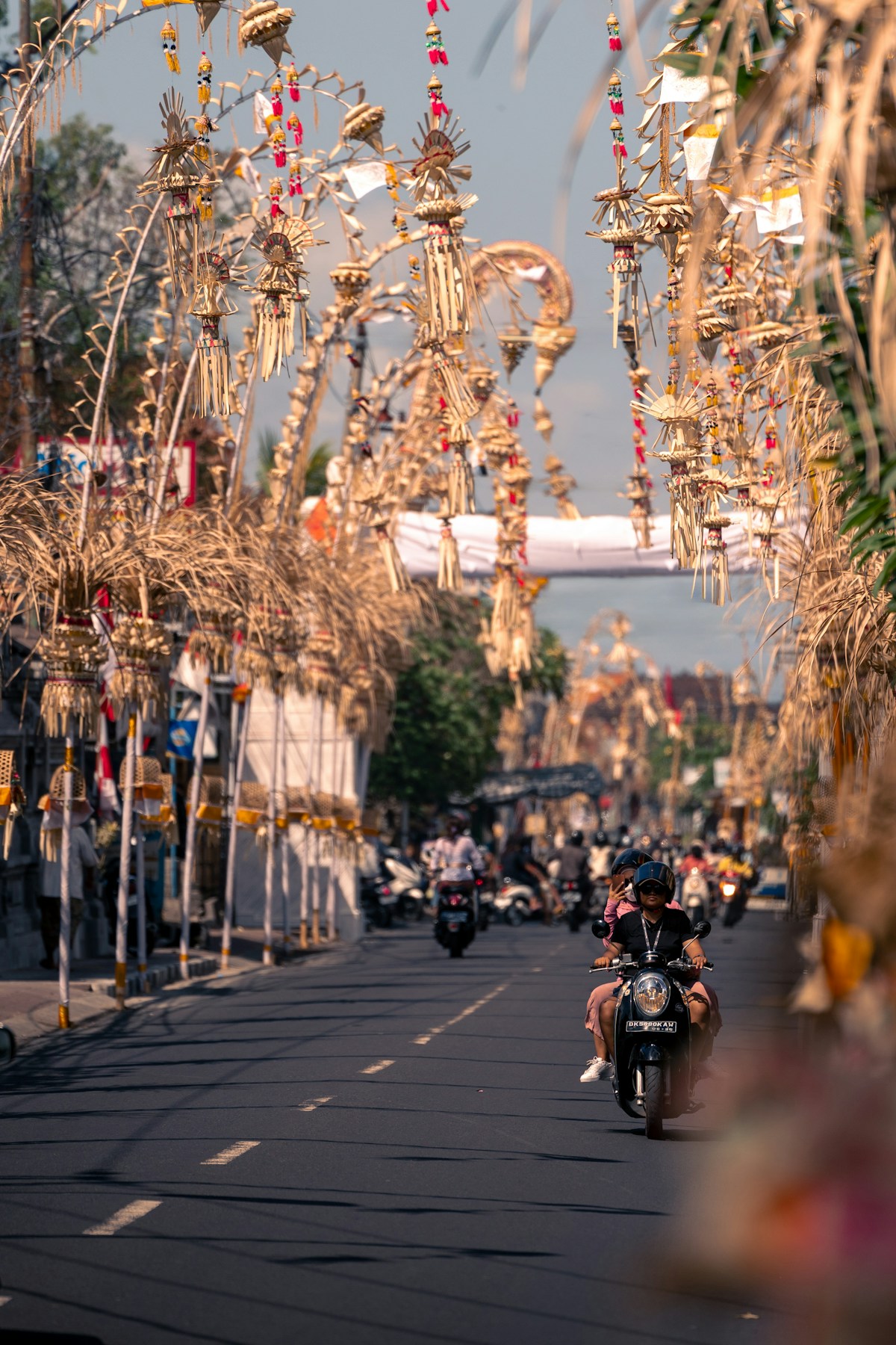 Street lined with Balinese penjor decorations and scooters in Bali, Indonesia