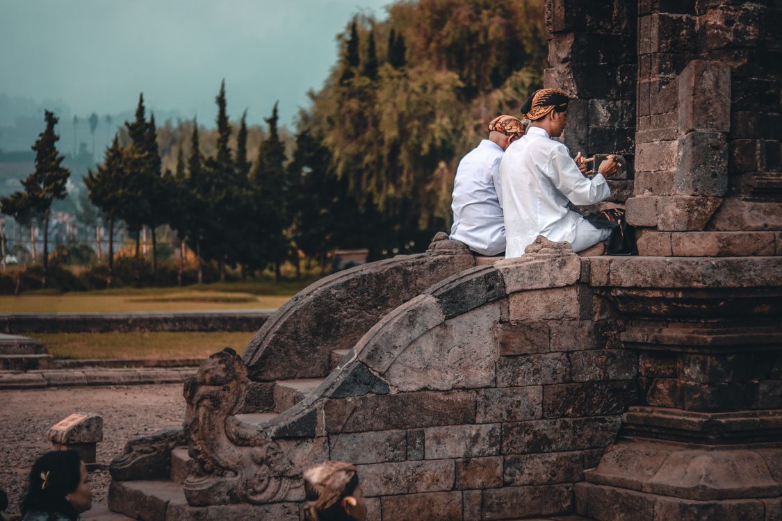 Two men in traditional Javanese dress praying at an ancient stone temple in Indonesia