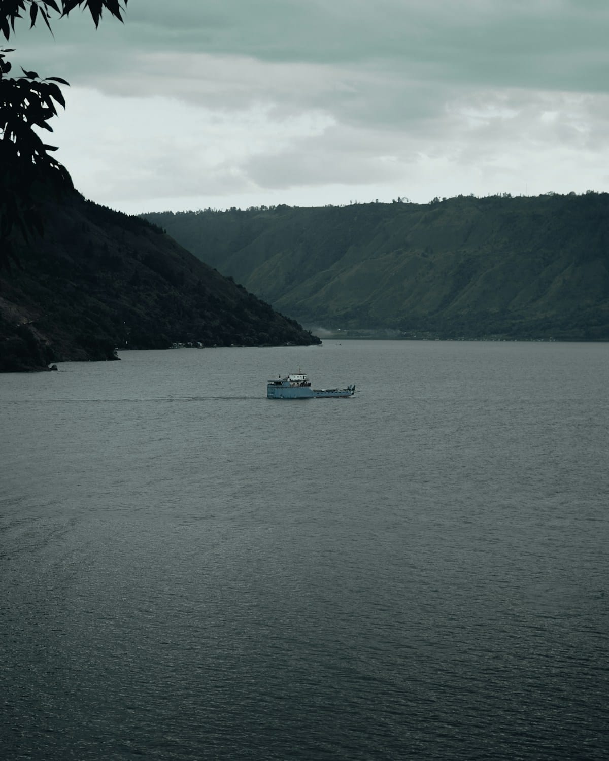 Small ferry crossing Lake Toba with green mountain ridges behind, North Sumatra, Indonesia