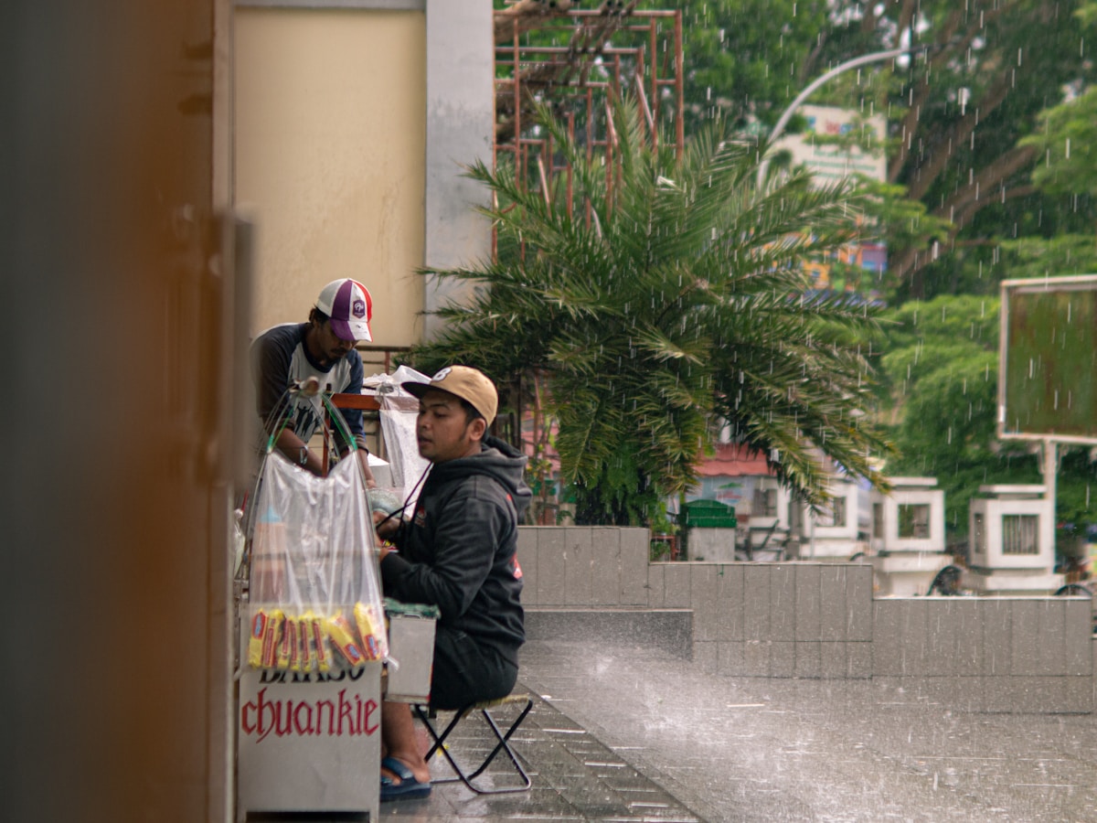 Two men at a street vendor during a downpour, Garut, West Java, Indonesia