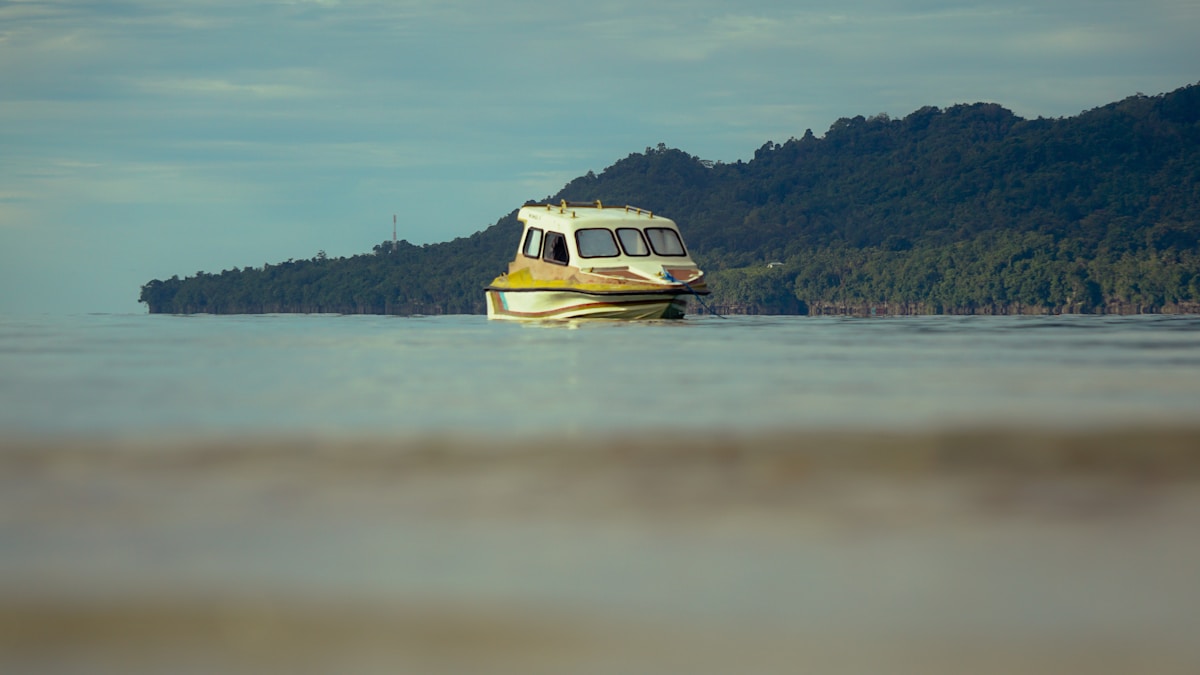 Wooden ferry boat on calm bay with forested hills, Ambon, Maluku, Indonesia