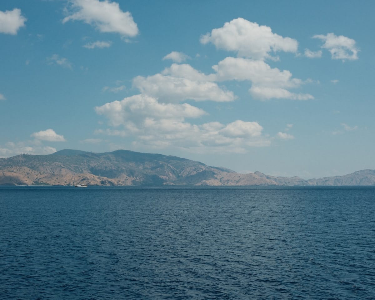 Deep blue sea with volcanic hills and a small ferry in the distance, Ende Bay, Flores, Indonesia