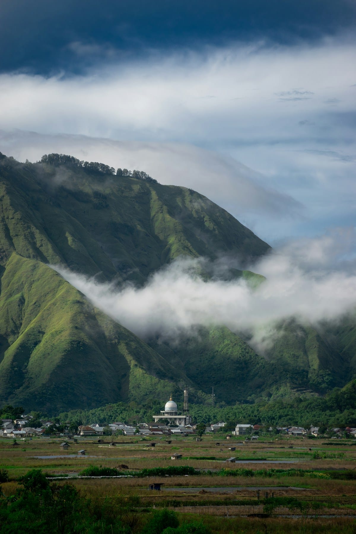 Mosque dome and traditional settlement surrounded by lush green mountains and low cloud, Lombok, Indonesia