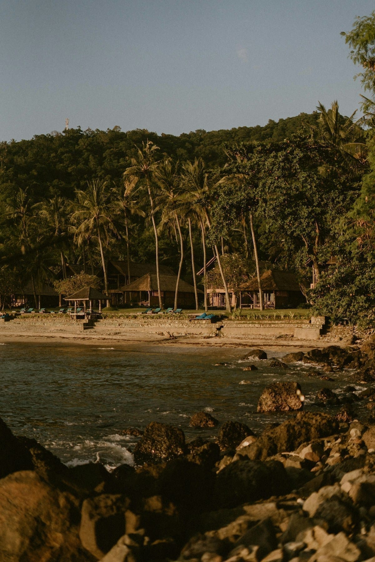 Beach resort with thatched bungalows and palm trees at golden hour, Senggigi, Lombok, Indonesia