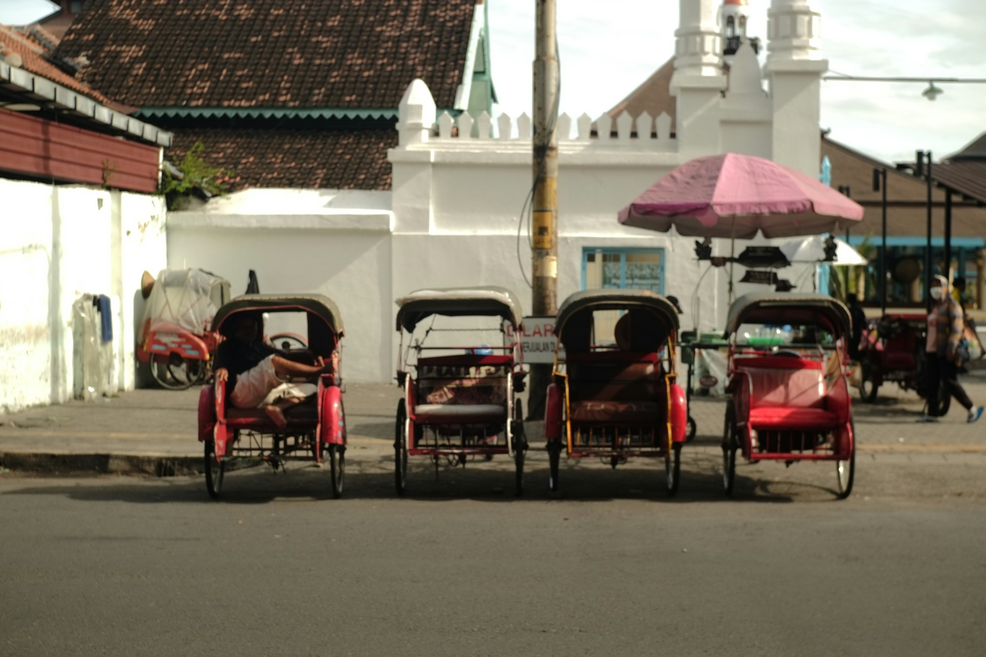 Becak rickshaws lined up in a Solo street near white historic buildings, Surakarta