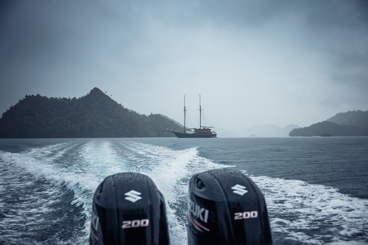Speedboat leaving a wooden liveaboard vessel in a remote island bay, Raja Ampat, West Papua, Indonesia