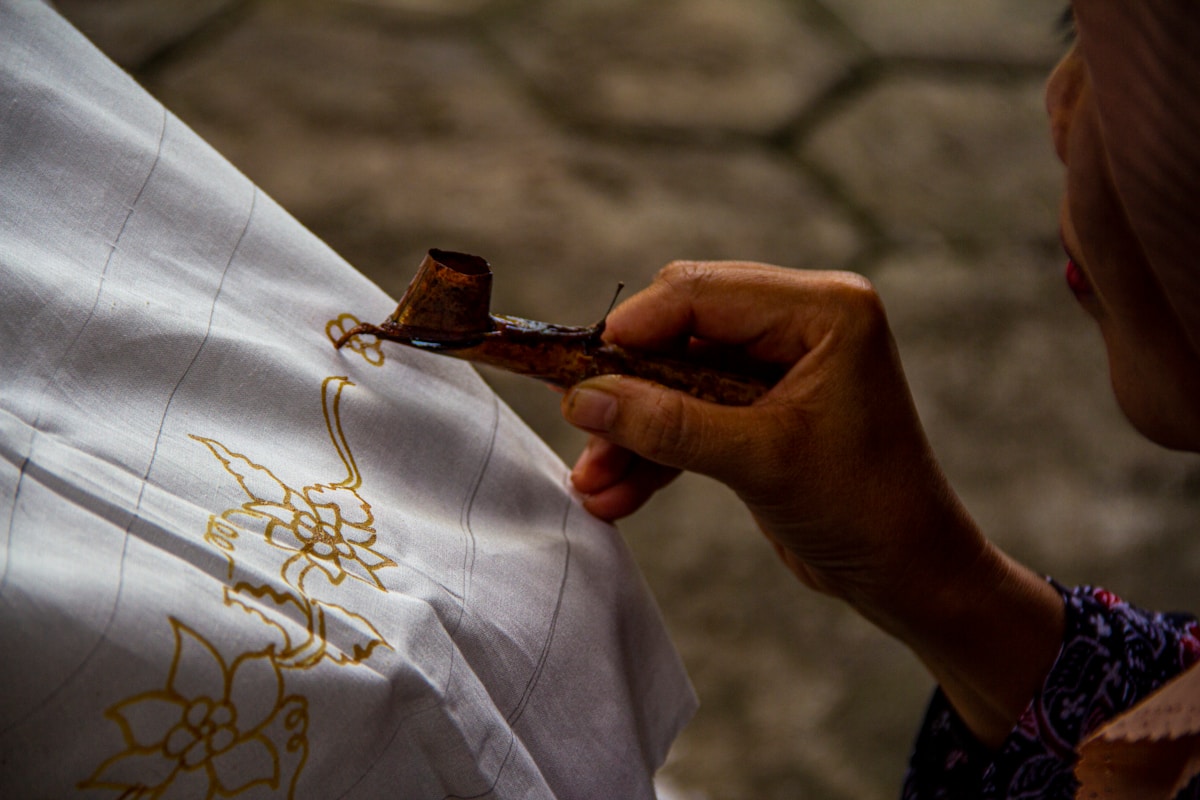 A batik craftsperson applying hot wax to fabric using a canting tool in a Yogyakarta workshop